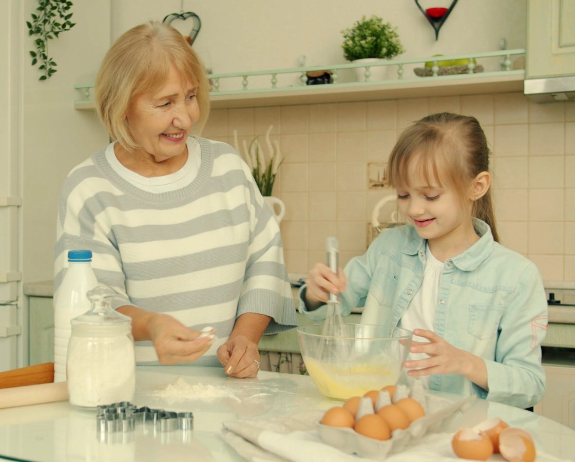 A grandmother and her granddaughter baking together at the kitchen table